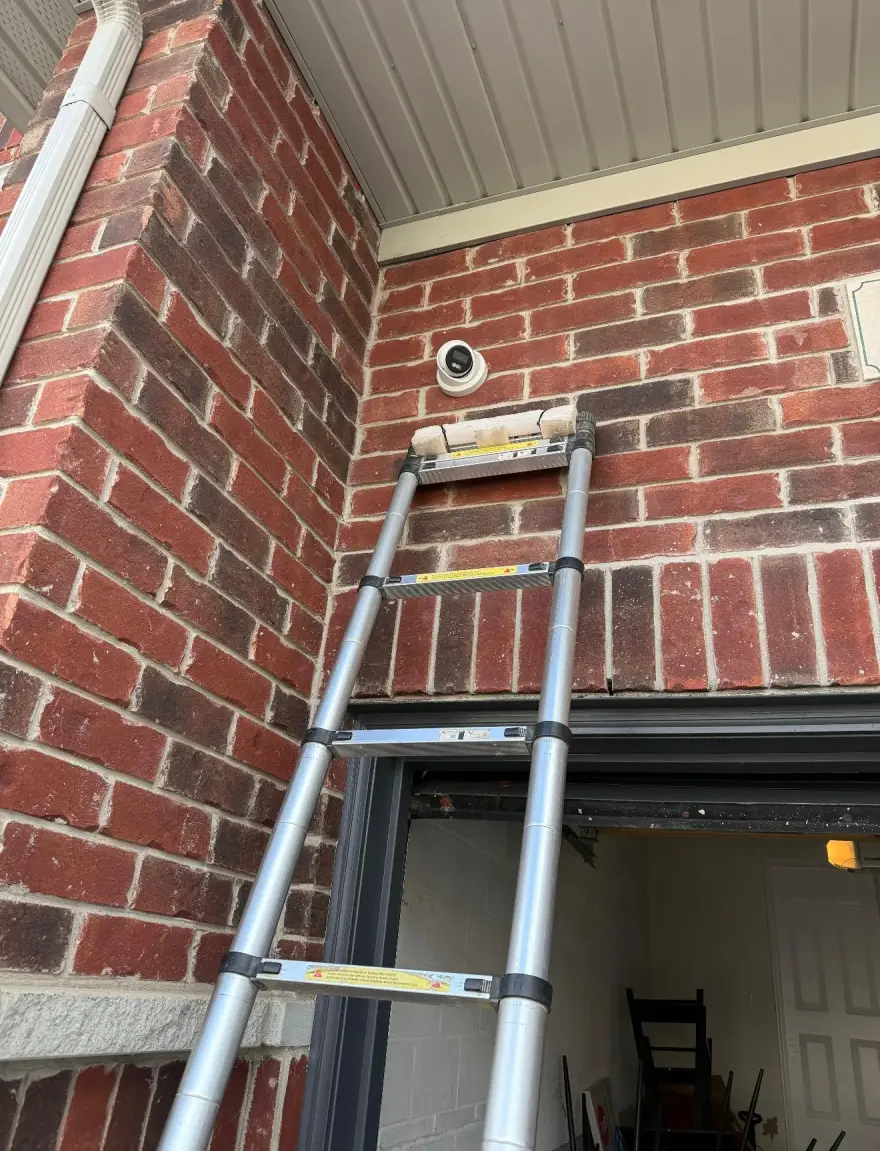 Telescoping ladder set against a Durham brick home with a 4K dome camera freshly mounted above the garage door area.